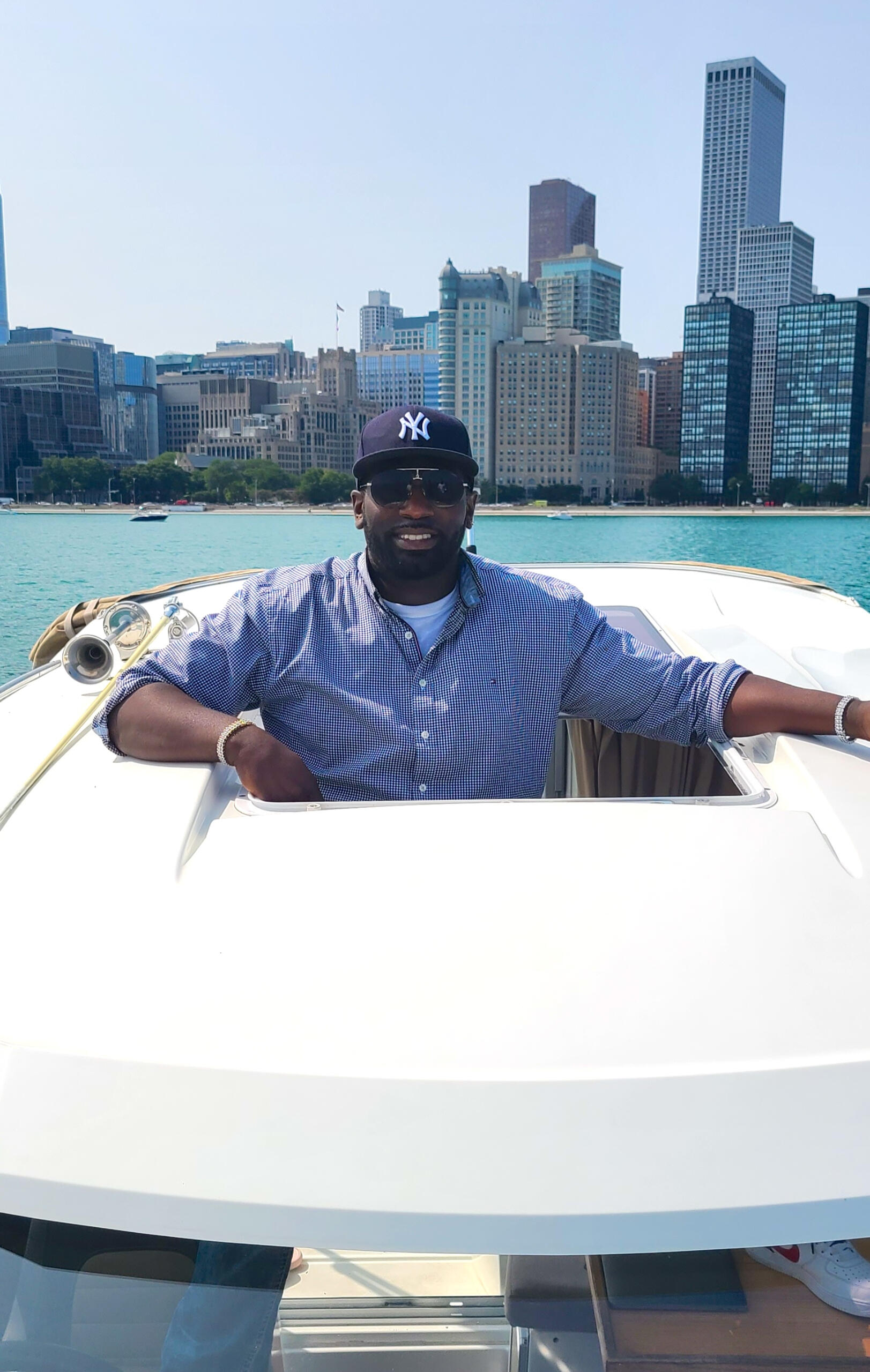 Micah Berkley in a white suit and black NY cap, with a high-rise cityscape backdrop, exuding confidence and urban sophistication.