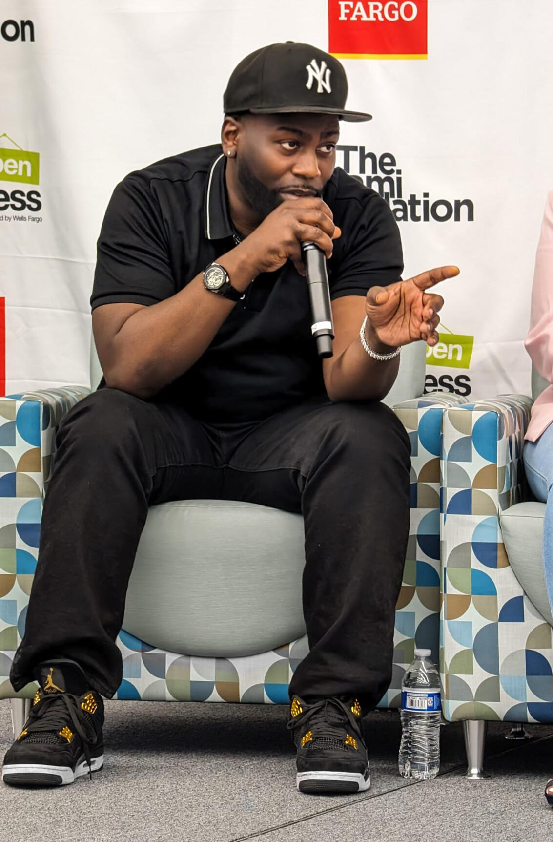 Micah Berkley in a white suit and black NY cap, with a high-rise cityscape backdrop, exuding confidence and urban sophistication.